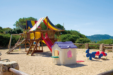 Speelplein met glijbaan, speelhuisje en zand in Centro Vacanze Isuledda vakantiepark op Sardinië, Italië.