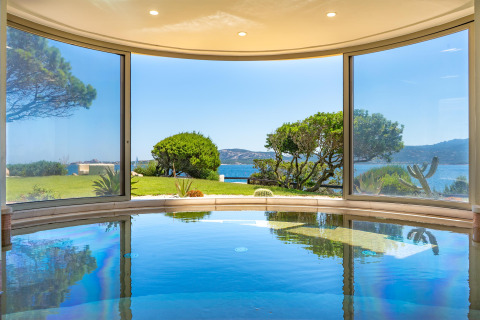 Indoor pool with panoramic windows overlooking the garden, sea and hills at Centro Vacanze Isuledda, Sardinia.