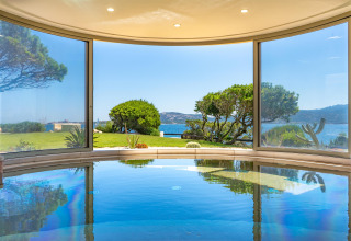Piscine intérieure avec baies vitrées et vue panoramique sur jardin, mer et collines à Isuledda, Sardaigne.