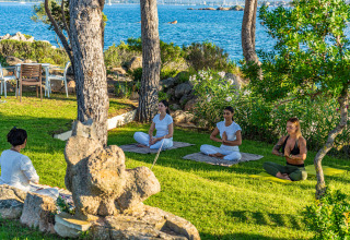 Personen beoefenen yoga en meditatie aan zee bij Centro Vacanze Isuledda, een vakantiepark op Sardinië, Italië.