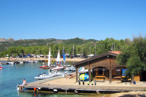 Vakantie op Centro Vacanze Isuledda in Sardinië met zeilboten, houten hut en helderblauw water.