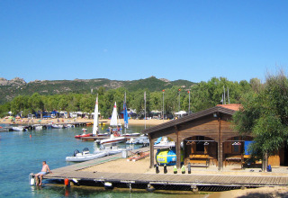 Vakantie op Centro Vacanze Isuledda in Sardinië met zeilboten, houten hut en helderblauw water.