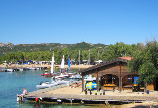 Feriebillede fra Centro Vacanze Isuledda i Sardinien med sejlbåde, en træhytte og klart blåt vand.
