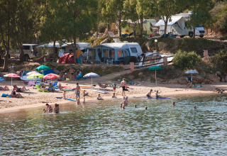 Feriecampingplads i Sardinien med familier, campingvogne og telte ved stranden samt folk der bader.
