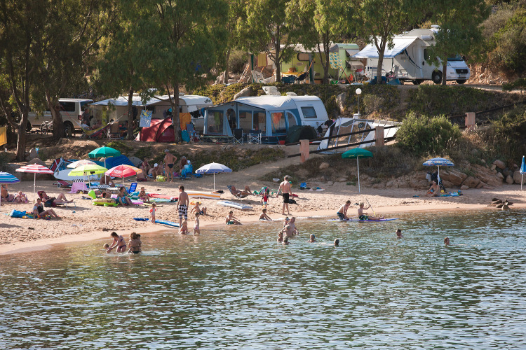 Gezinnen en kampeerders ontspannen op het strand van Centro Vacanze Isuledda met campers en tenten, Sardinië.