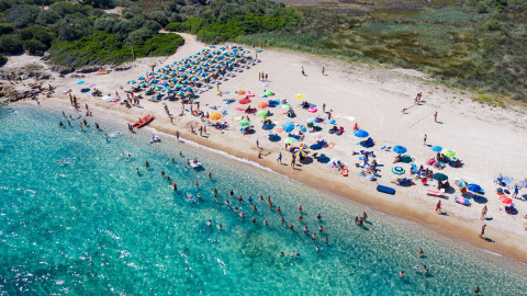 Vista aérea de la playa concurrida en Centro Vacanze Isuledda, Cerdeña, Italia, con sombrillas de colores.