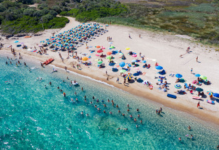 Luftfoto af travl strand ved Centro Vacanze Isuledda feriested, Sardinien, Italien med farverige parasoller.