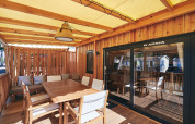 Covered lodge terrace with wooden table, chairs and cushions, ideal for outdoor dining and relaxation.