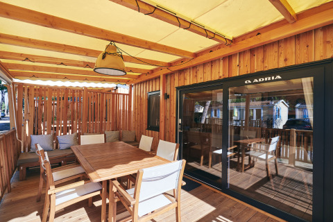 Udendørs terrasse på en lodge med træmøbler, puder og overdækning, ideel til afslapning og måltider.