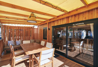 Covered lodge terrace with wooden table, chairs and cushions, ideal for outdoor dining and relaxation.