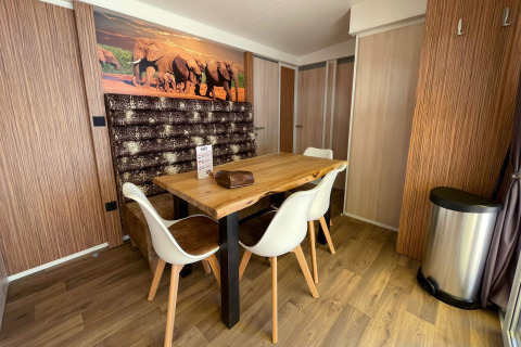 Coin repas moderne à SunLodge Sabai avec table en bois, chaises blanches, décor éléphants et sol en bois.