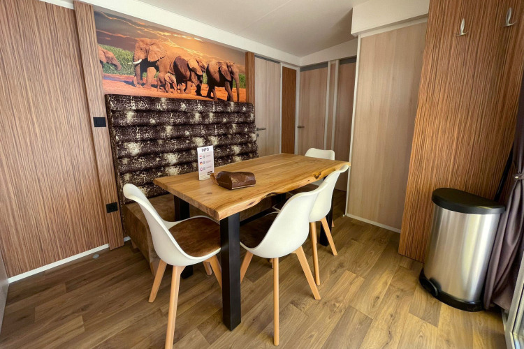 Comedor en SunLodge Sabai con mesa de madera, sillas blancas, decoración de elefantes y suelo de madera.