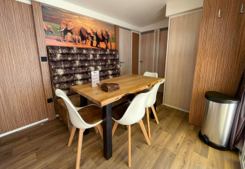 Coin repas moderne à SunLodge Sabai avec table en bois, chaises blanches, décor éléphants et sol en bois.