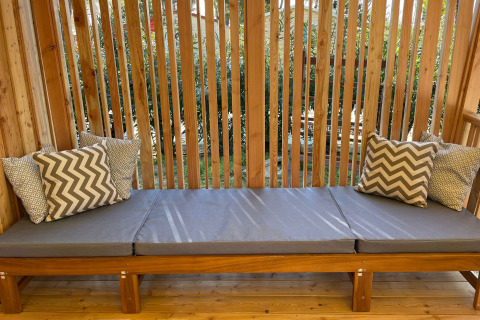 Banc extérieur en bois avec coussins gris et oreillers à motifs chez SunLodge Babul, Centro Vacanze Isuledda, Italie.