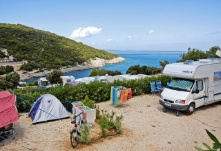 Campingplads ved kysten i Kroatien med telte og autocampere, udsigt over havet og grønne bakker.
