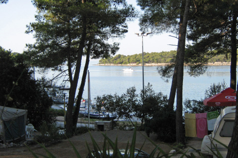 Vista al mar desde Camping Village Poljana en Croacia, con árboles, bote y ropa tendida al sol.