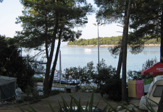 Seaside view from Camping Village Poljana in Croatia, showing trees, a boat, and laundry drying outside.
