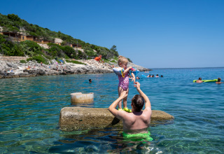 Un uomo solleva un bambino su una roccia nell'acqua limpida a Camping Village Poljana, Croazia, d’estate.