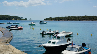 Barcos atracados en la orilla en Camping Village Poljana, Croacia, rodeados de agua tranquila y colinas verdes.