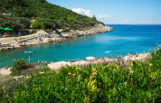 Camping Village Poljana in Croatia with visitors enjoying clear blue water, green hills and rocky beach.