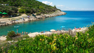 Camping Village Poljana in Kroatië, bezoekers genieten van helderblauw water, groene heuvels en strand.