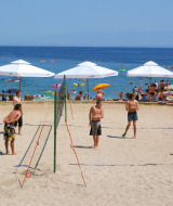 Parque vacacional en Croacia con personas jugando vóley playa en la arena junto al mar y sombrillas.