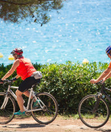 Dos ciclistas con cascos pedalean junto a la costa cerca de Mali Losinj, Croacia, frente al mar azul.