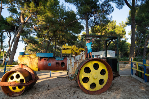 Bambino su uno schiacciasassi colorato al Camping Village Poljana, Croazia, immerso tra alberi verdi.