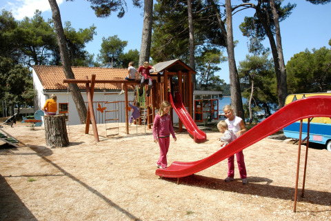 Niños jugando en un parque infantil en Camping Village Poljana, rodeados de árboles en Croacia.