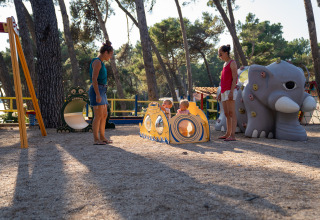 Bambini che giocano al parco giochi con genitori al Camping Village Poljana, Croazia, tra alberi.