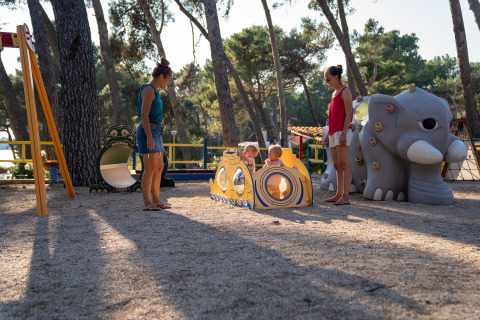 Niños jugando en un parque infantil con padres en Camping Village Poljana, Croacia, rodeados de árboles.