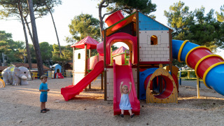 Niños juegan en un colorido parque infantil rodeado de árboles en Camping Village Poljana, Croacia.