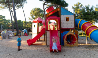 Niños juegan en un colorido parque infantil rodeado de árboles en Camping Village Poljana, Croacia.