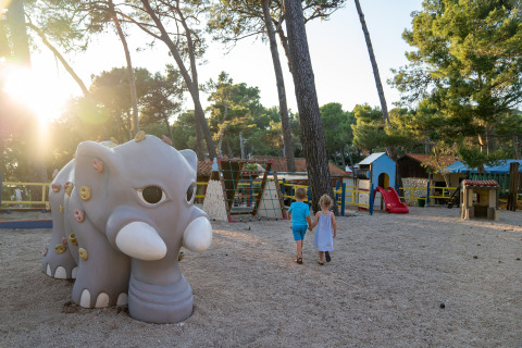 Dos niños caminan de la mano por un parque infantil con un elefante en Camping Village Poljana, Croacia.