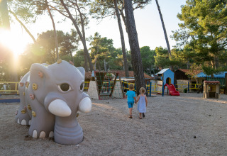 Deux enfants marchent main dans la main sur une aire de jeux avec un éléphant au Camping Village Poljana, Croatie.
