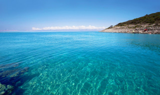 Aguas turquesas y cristalinas cerca de Mali Losinj, Croacia, con costa rocosa y cielo despejado.