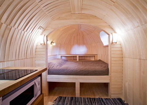 Interiør af IGLO Log Cabin på Camping Emmen i Holland, med trævægge, seng og lille køkkenhjørne.