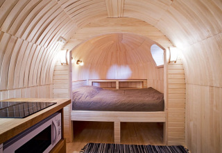 Interiør af IGLO Log Cabin på Camping Emmen i Holland, med trævægge, seng og lille køkkenhjørne.