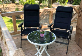 Deux chaises noires et une table avec une fleur sur la terrasse d’IGLO Log Cabin, Camping Emmen, Pays-Bas.