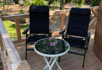 Zwei schwarze Stühle und ein Tisch mit Blume auf der Terrasse der IGLO Log Cabin, Camping Emmen, Niederlande.