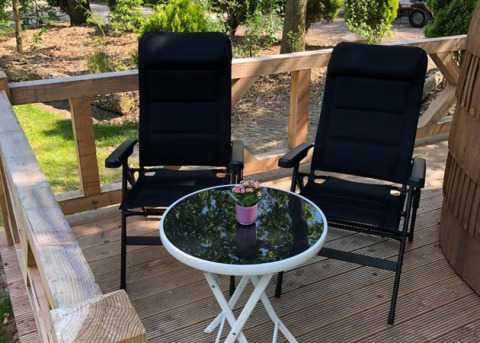Two black chairs and a table with a flower pot on the terrace at IGLO Log Cabin, Camping Emmen, Netherlands.