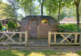 Cabane en forme d'igloo en bois au Camping Emmen, Pays-Bas, entourée d'arbres et d'une barrière en bois.
