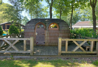 Houten iglohut bij Camping Emmen in Nederland, tussen bomen en een houten hekwerk.