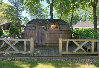 Houten iglohut bij Camping Emmen in Nederland, tussen bomen en een houten hekwerk.