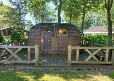 Capanna in legno a forma di igloo al Camping Emmen, Paesi Bassi, tra alberi e recinto di legno.