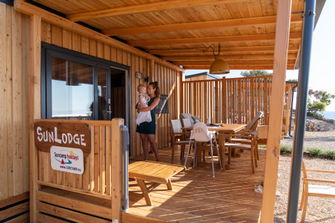 Porche de madera en SunLodge BigLeaf con mujer y niño, mesa de comedor y sillas al aire libre.