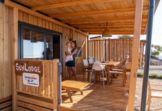 Porche de madera en SunLodge BigLeaf con mujer y niño, mesa de comedor y sillas al aire libre.
