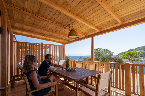 Dos personas se relajan en una terraza de madera con vistas al mar en SunLodge BigLeaf, Camping Village Poljana, Croacia.