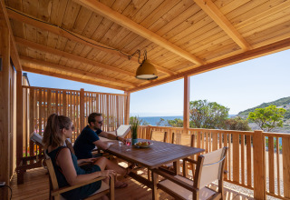 Dos personas se relajan en una terraza de madera con vistas al mar en SunLodge BigLeaf, Camping Village Poljana, Croacia.