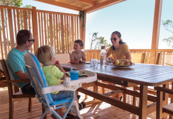 Famiglia che si gode un pasto insieme sulla terrazza in legno della SunLodge BigLeaf in una giornata soleggiata.